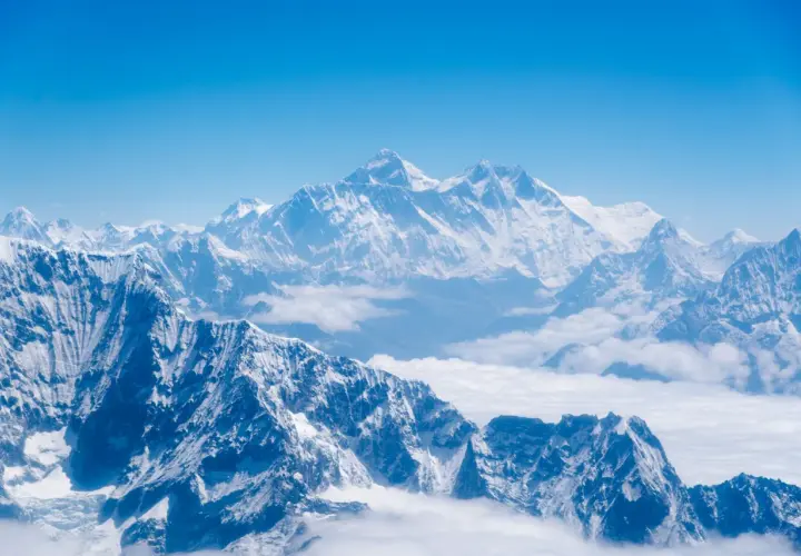 Majestatyczne, ośnieżone szczyty Himalajów, gdzie leży Mount Everest, wyłaniają się z morza chmur pod błękitnym niebem.