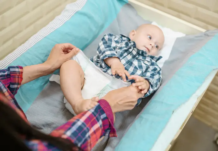 Mama zmienia pieluszkę maluszkowi. Dobór odpowiednich rozmiarów pampersów jest kluczowy dla komfortu dziecka.