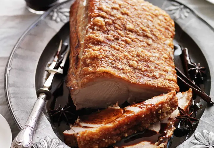 Poitrine de porc croustillante, dorée et juteuse, servie sur une assiette ornée avec des épices.