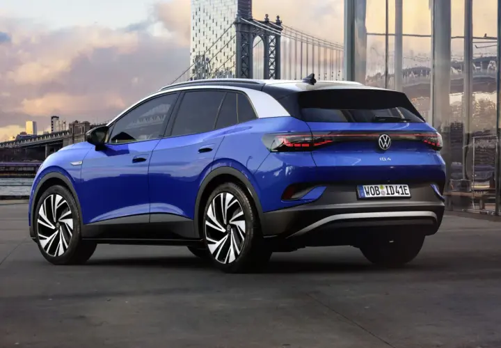 Niebieski Volkswagen ID.4 z białym dachem, zaparkowany na tle miasta z mostem i nowoczesnymi budynkami.