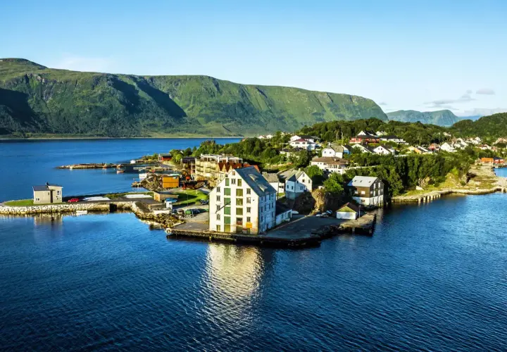Malowniczy widok na Ålesund Vigra z domkami nad wodą i zielonymi wzgórzami w tle.