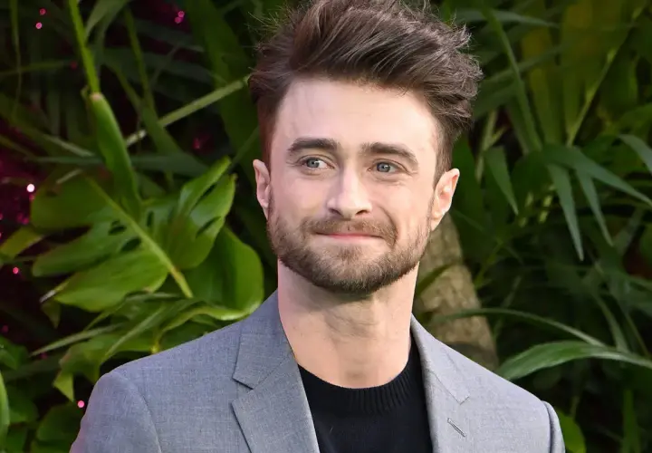 Daniel Radcliffe, który grał Harry'ego Pottera, w szarym garniturze na tle zieleni.