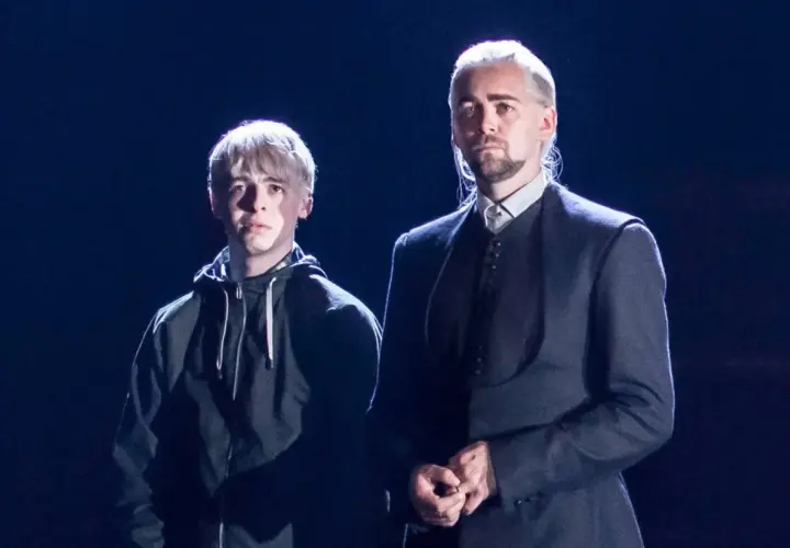 Scorpius Malfoy w czarnej bluzie obok starszego mężczyzny w eleganckim stroju.