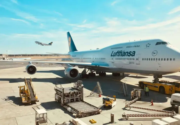 Lufthansa bagaż podręczny czeka na załadunek obok gigantycznego Boeinga 747-400 na lotnisku.