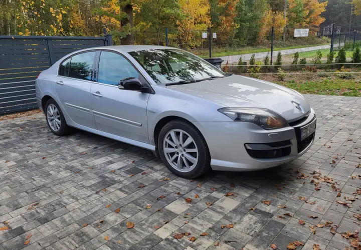 Srebrny sedan Laguna 3 2.0 dCi zaparkowany na podjeździe z kostki brukowej, otoczony jesienną roślinnością.