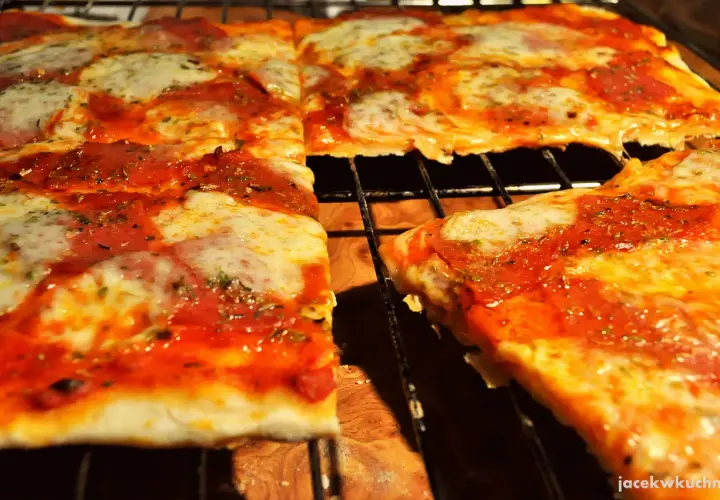 Pyszna pizza na cienkim cieście, z sosem pomidorowym i ciągnącym się serem, pokrojona na kwadraty.
