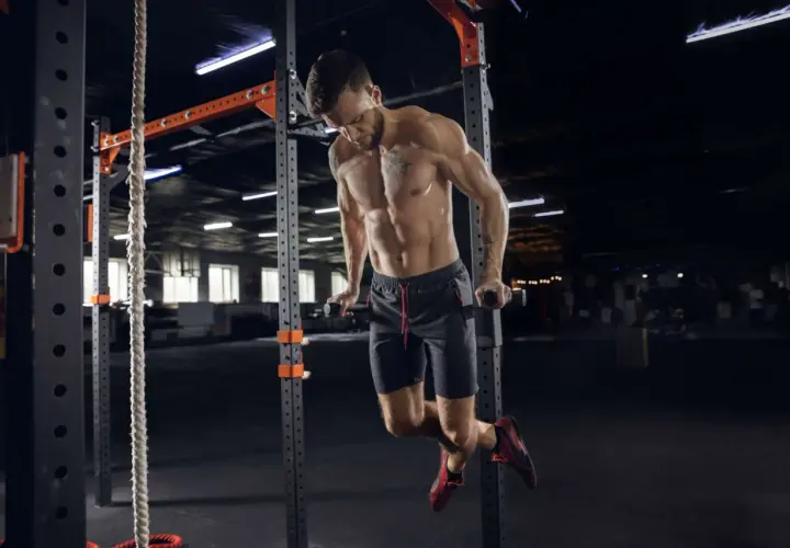 Mężczyzna wykonuje pompki na poręczach w siłowni CrossFit.