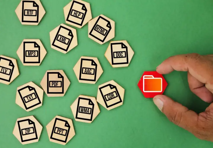Un dedo toca una carpeta roja, rodeada de fichas de madera con extensiones de archivo como ZIP, MP3, DOC, etc. que representan un archivo comprimido.