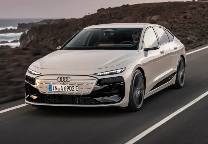 Elegancki Audi A6 e-tron w kolorze kremowym przemierza malowniczą, nadmorską drogę.