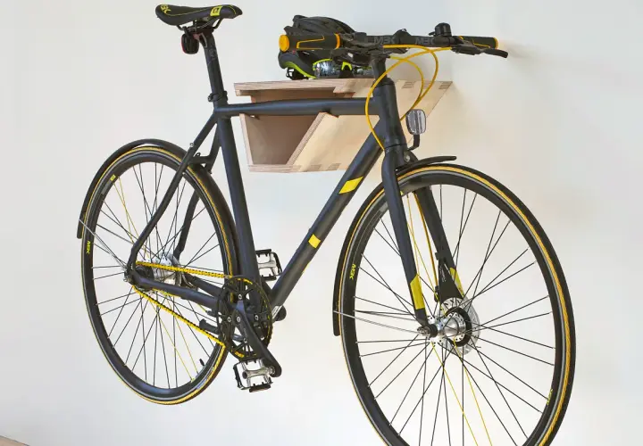 Schwarzes Fahrrad mit gelben Akzenten hängt an einer selbstgebauten Holz-Fahrrad-Wandhalterung. Helm liegt auf der Ablage.