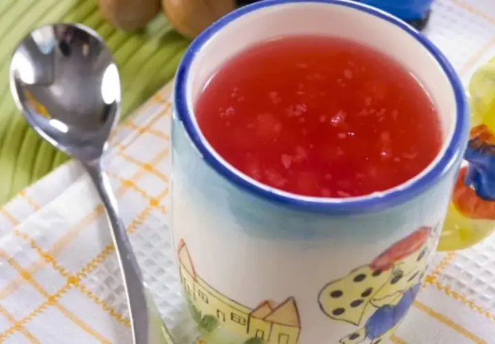 Czerwony kisiel na diecie w kubeczku z bajkowym wzorem, obok łyżeczka. Idealny na lekki deser.