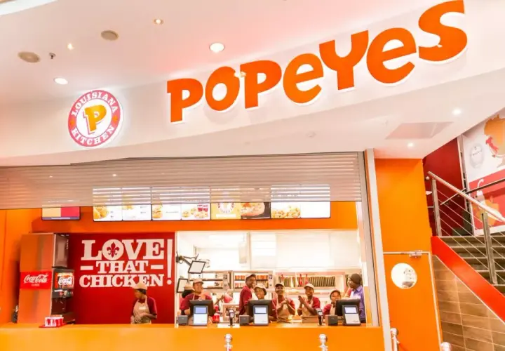 Wnętrze restauracji Popeyes Polska. Pracownicy za ladą, logo "Love That Chicken" i menu.