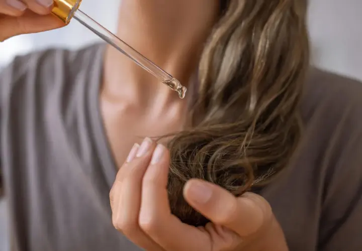 Una gota de aceite de aguacate para el pelo cae de un gotero sobre un mechón de cabello.