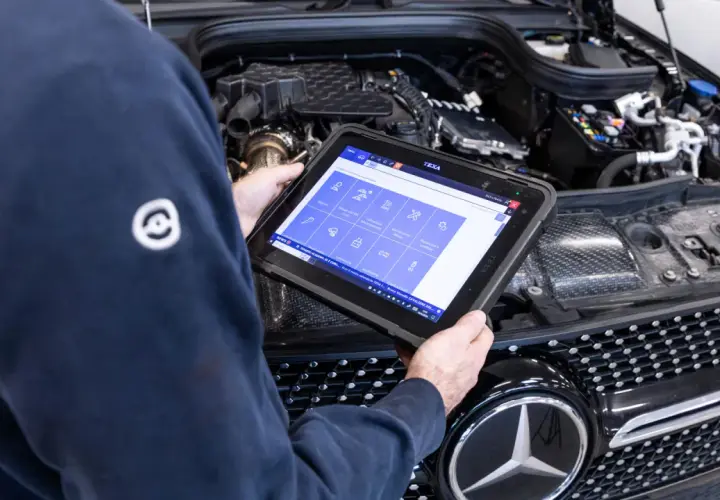 Meccanico esegue la prima revisione auto con tablet diagnostico davanti al motore di una Mercedes.