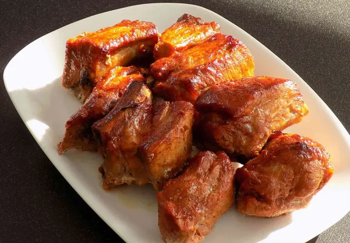 Żeberka pieczone, błyszczące od sosu z marynaty do żeberek, ułożone na białej tacy.