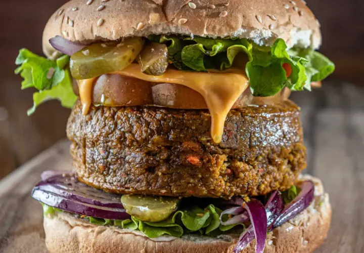 Deliciosa hamburguesa vegana con queso derretido, lechuga fresca, pepinillos y cebolla morada.