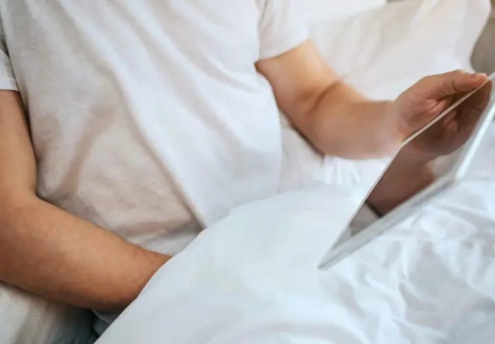 Persona in letto con tablet, forse cercando informazioni su che significa masturbare.