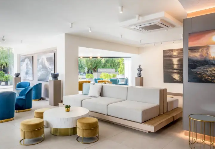 Salón moderno con sofás modulares, sillones azules y arte marino. El cartel "Occidental Puerto Banús" se ve al fondo.