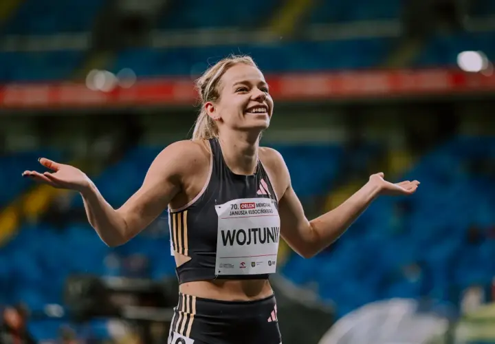 Uśmiechnięta Klaudia Wojtunik z rozłożonymi rękami na stadionie, celebrująca sukces.