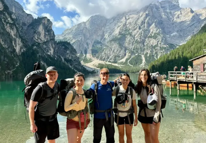 Cinco excursionistas sonríen junto a un lago turquesa con imponentes montañas de **Alta Ribagorza** al fondo.