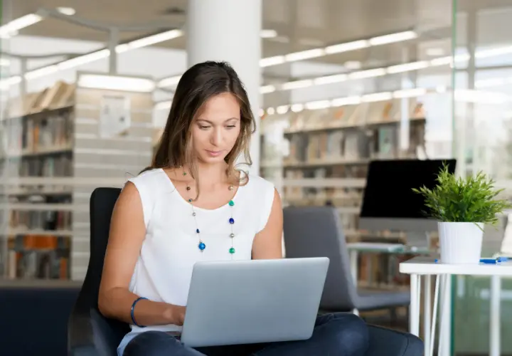 Kobieta siedzi w bibliotece, ucząc się, jak założyć PUE ZUS na laptopie.