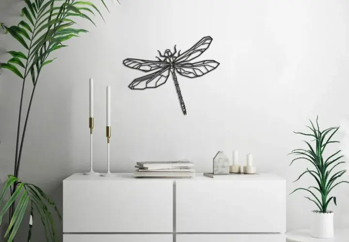 Un moderno cuadro de libélula adorna la pared blanca, sobre un mueble blanco con plantas y velas.