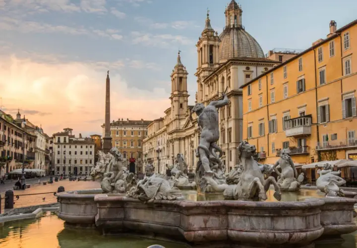 Fontana dei Quattro Fiumi a Piazza Navona, con l'obelisco e la chiesa di Sant'Agnese in Agone sullo sfondo, al tramonto.