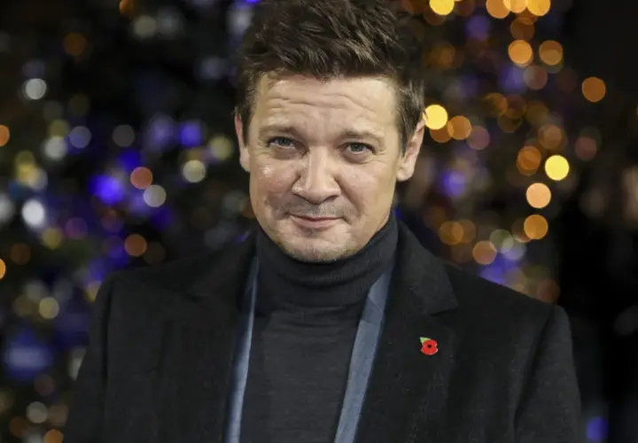 Jeremy Renner, med en vallmo på kavajen, ser allvarlig ut mot en bakgrund av julbelysning. Efter sin svåra olycka är han tillbaka.