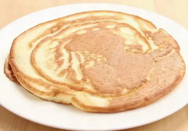Ein goldbrauner Pfannkuchen ohne Ei auf einem weißen Teller, perfekt für ein leichtes Frühstück.