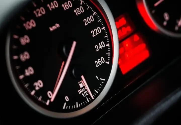 Zbliżenie na deskę rozdzielczą samochodu: prędkościomierz pokazuje 80 km/h, a obok wskaźnik paliwa wskazuje prawie pełny bak.