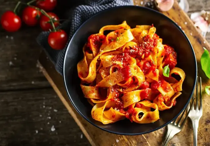 Pappardelle z sosem pomidorowym, świeże pomidory i bazylia. Pyszne dania z pomidorów na drewnianym blacie.
