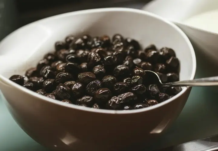 Un cuenco blanco lleno de aceitunas negras brillantes, perfecto para tus recetas con aceitunas negras.