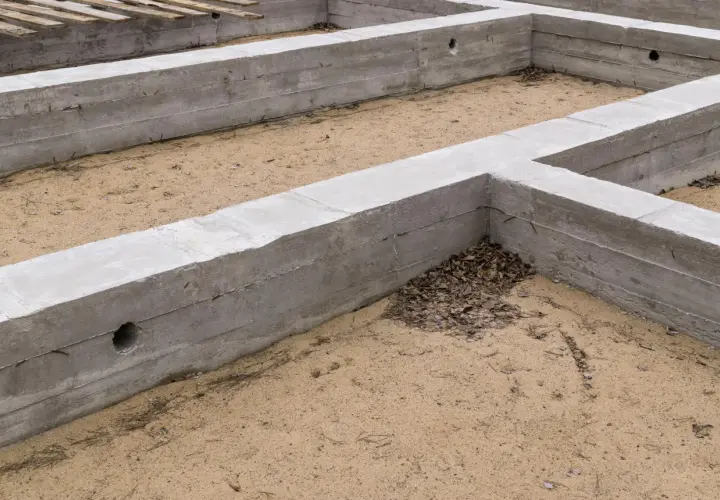 Betonowe fundamenty tworzą zarys przyszłego domu. To stan zero budynku, gdzie piasek i liście tworzą naturalne wypełnienie.