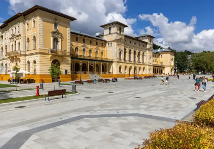 Plac przed zabytkowym sanatorium. Ludzie spacerują, odpoczywają na ławkach. Może to miejsce, gdzie czekają na nowe zasady wyjazdu do sanatorium na NFZ.