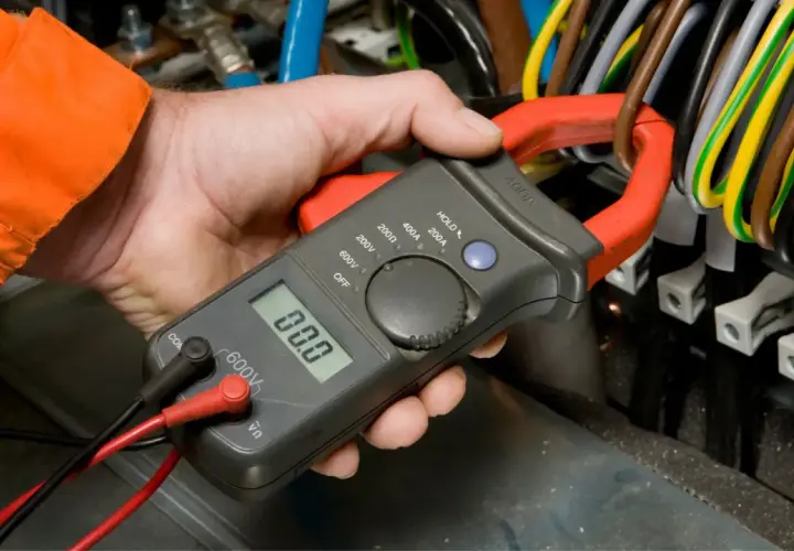 Elektryk mierzy prąd szczypcami cęgów, sprawdzając dopuszczalny spadek napięcia na przewodach.