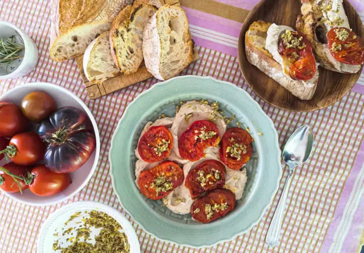 Tomates italianos asados sobre una crema suave, acompañados de pan rústico y tomates frescos.