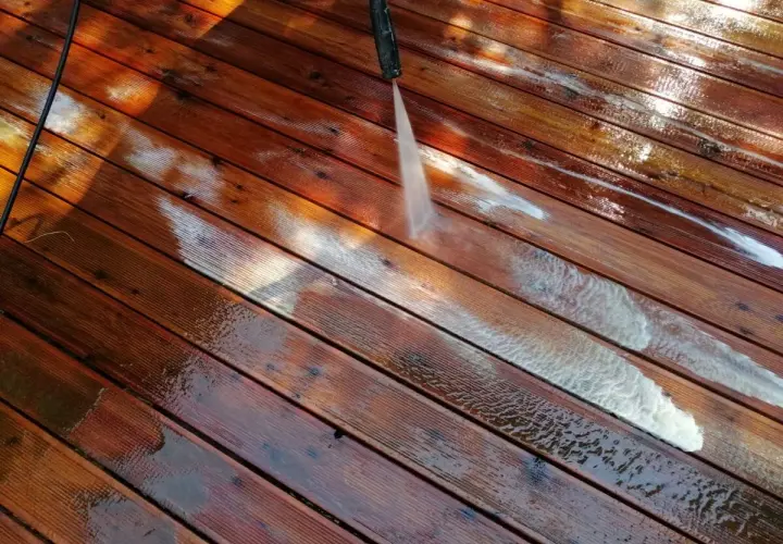 Mycie tarasu wodą pod ciśnieniem to jeden ze sposobów, jak usunąć farbę z drewna domowe sposoby. Woda spływa po deskach.