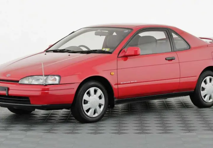 Czerwone, dwudrzwiowe Toyota Paseo z lat 90. na szarym, kratkowanym tle.