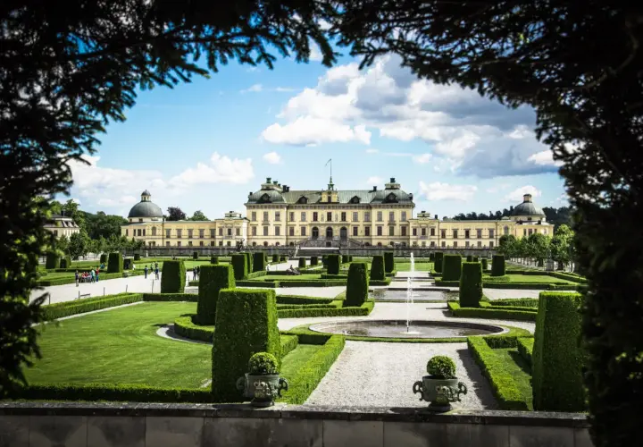 Drottningholms slottspark med fontäner och välklippta häckar. Kanske kungens båt ligger vid kajen, redo för en tur.