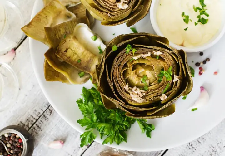 Deliciosas alcachofas al horno, tiernas y doradas, servidas con una cremosa salsa y perejil fresco. Un plato perfecto para disfrutar.
