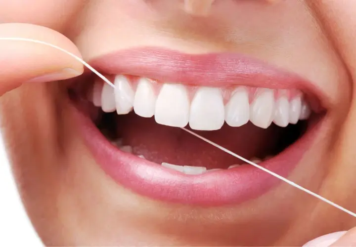 Dita che usano il filo interdentale per pulire i denti bianchi e perfetti. Un gesto quotidiano per un sorriso smagliante.