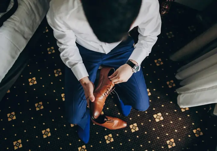 Mężczyzna w niebieskim garniturze i białej koszuli zakłada brązowe, eleganckie buty. Idealne pytanie: jakie buty do niebieskiego garnituru?