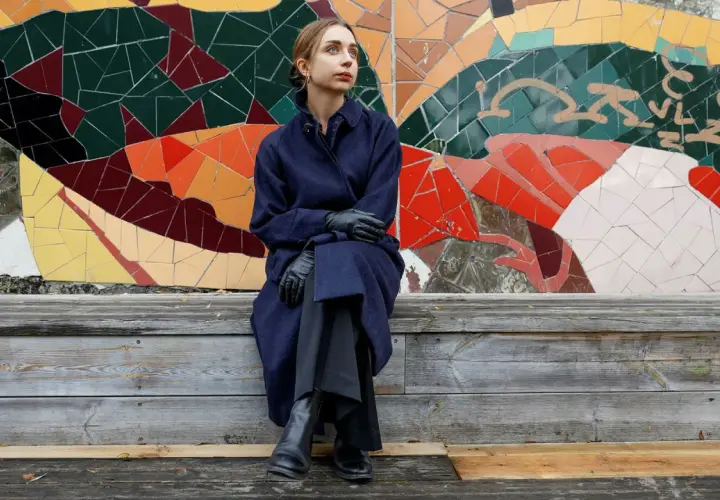 Alexandra Andersson sitter på en träbänk framför en färgglad mosaikvägg.
