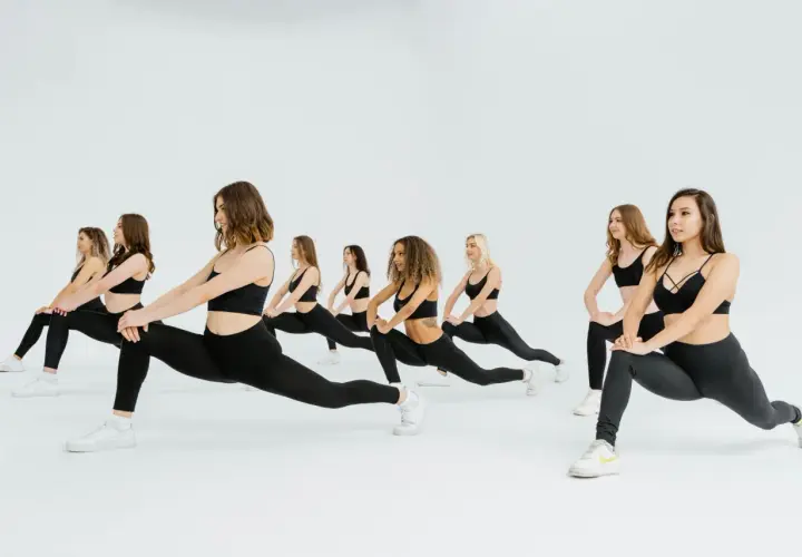 Grupo de mujeres realizando estocadas, parte de **15 ejercicios de calentamiento** para preparar el cuerpo.