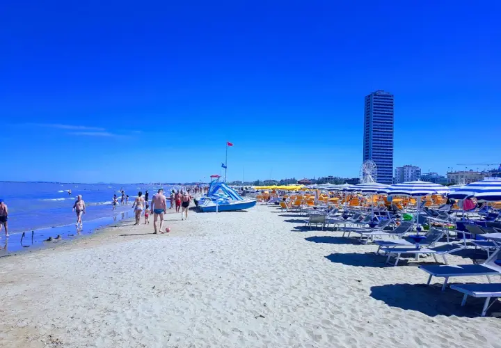 Plage animée à Cesenatico, Italie, avec des parasols rayés, des chaises longues et des baigneurs profitant du soleil sous un ciel bleu éclatant.