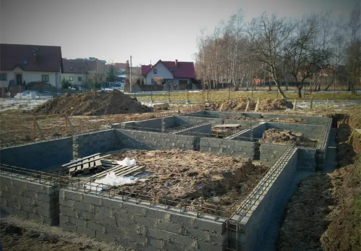 Budowa fundamentów domu w trakcie. Widać zbrojenie i bloczki betonowe, przygotowywane pod izolację poziomą fundamentów.