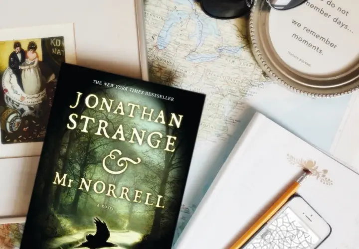 Książka "Jonathan Strange i Pan Norrell" leży obok mapy, telefonu i okularów, gotowa na podróż pełną magii.