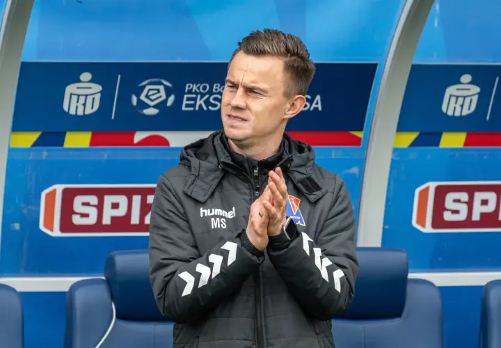Trener z PKO BP Ekstraklasa w TVP, kiedy? Mężczyzna w kurtce z logo "hummel" klaszcze na ławce rezerwowych.