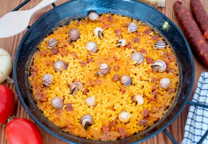 Arroz con caracoles, un plato tradicional español, se presenta en una paellera, adornado con caracoles y trozos de chorizo.