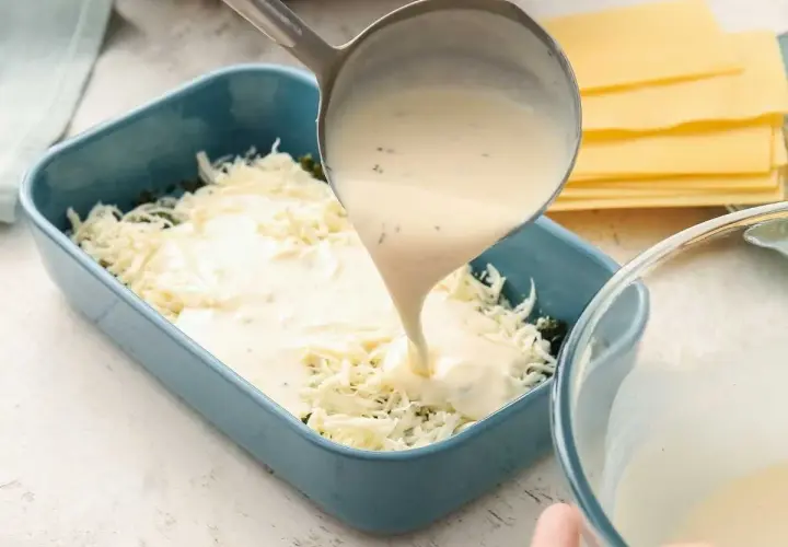 Se vierte bechamel para lasaña sobre queso rallado en un molde azul.